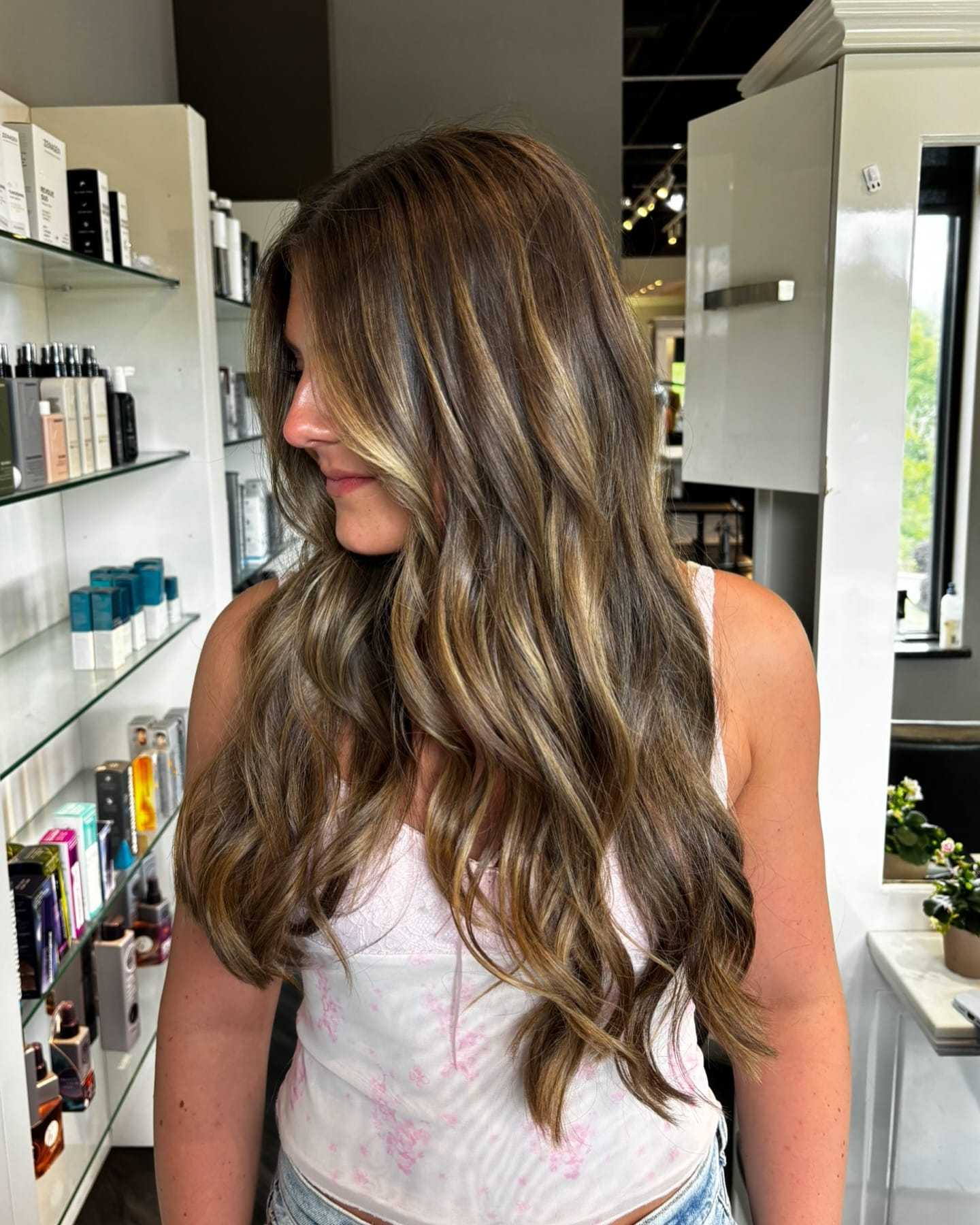 Long-haired woman with blonde highlights at a salon, wearing a floral top.