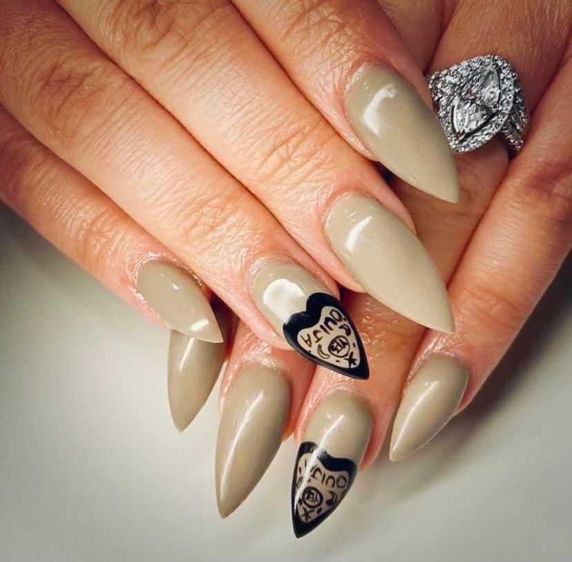 Beige stiletto nails with black heart design on ring fingers.