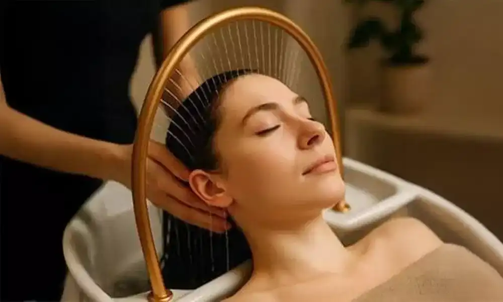Woman receiving a relaxing head massage under a golden water feature at a spa.